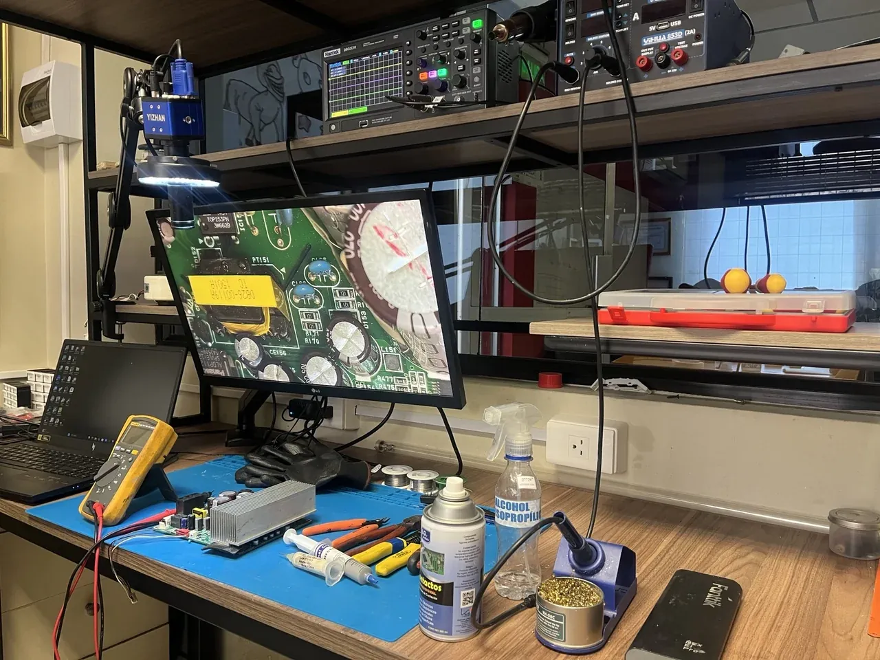 Mesa de trabajo del taller de RC Solutions en Guayaquil con multímetro, estación de soldadura, fuente de alimentación y monitor de inspección mostrando una tarjeta electrónica