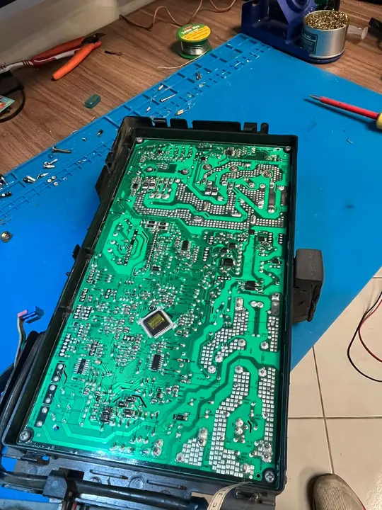 Tarjeta de unidad exterior inverter dentro de su bandeja plástica, vista por el lado de soldaduras sobre el tapete de trabajo